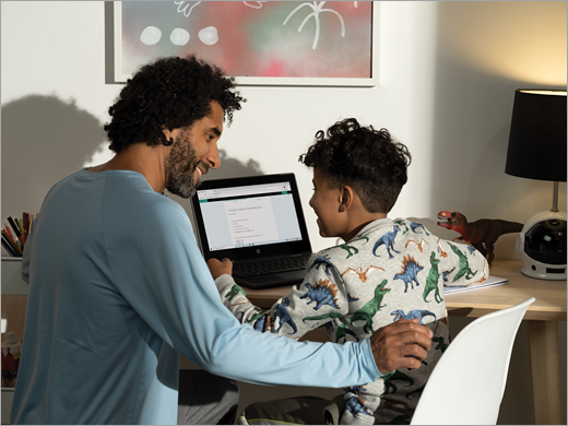 A father and son sit at a computer together, smilling