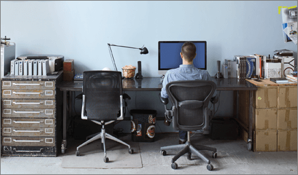 Photograph of a man sitting at a desk, working on a computer.