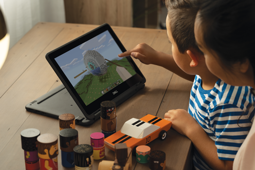 A young boy uses Minecraft on a laptop while a woman watches over his shoulder