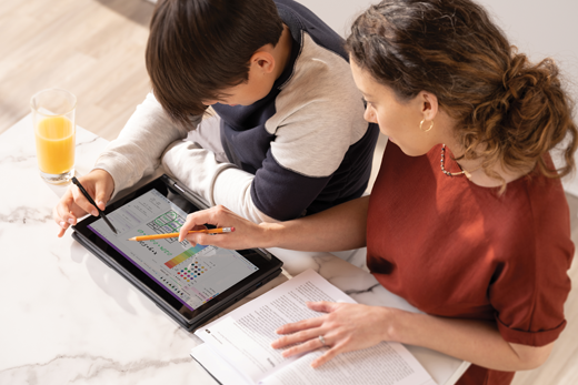 Un enfant masculin travaille sur une tablette tandis que son parent féminin regarde par-dessus son épaule