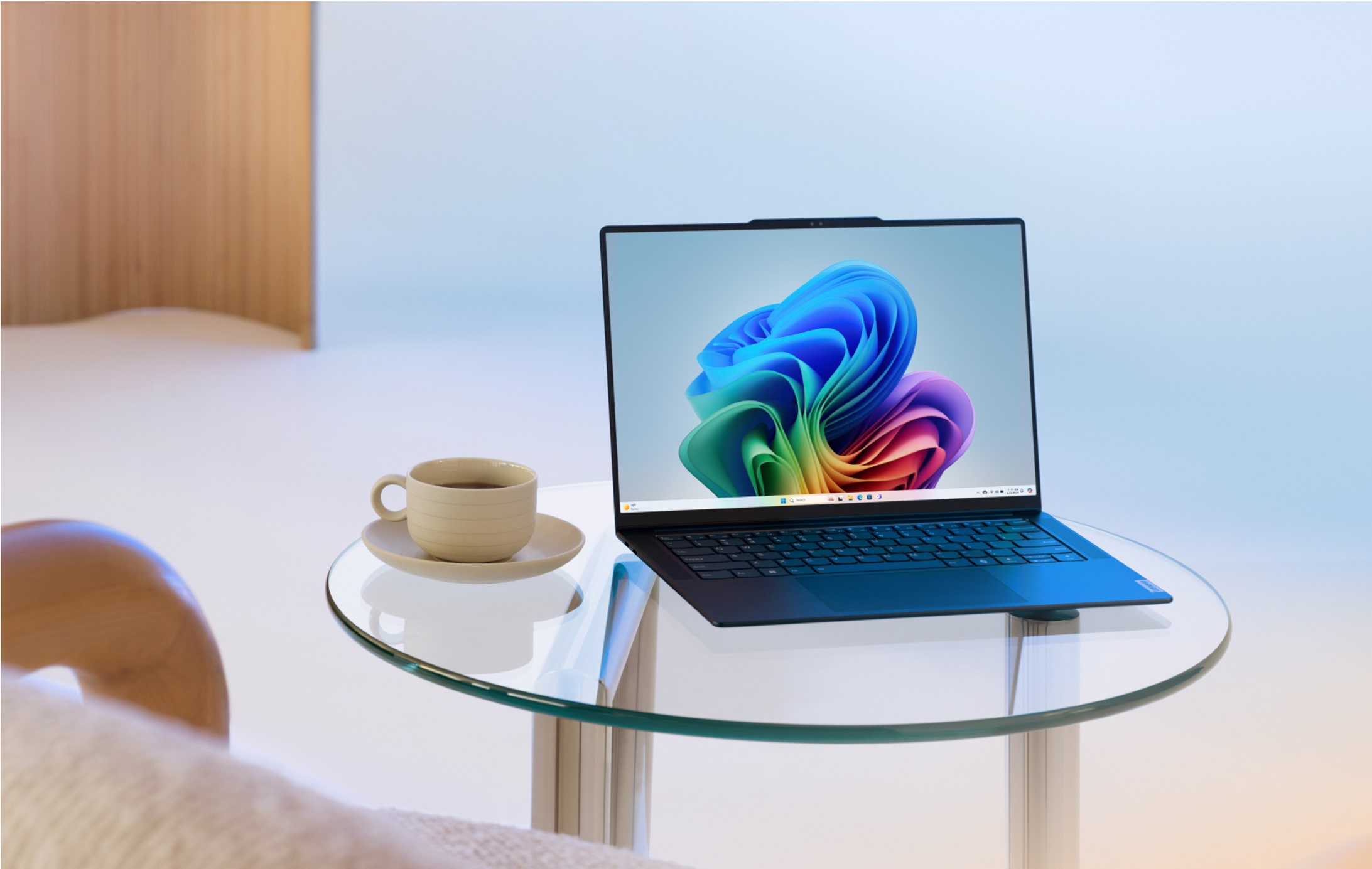 Un PC Windows 11 affichant l’arrière-plan de bureau à fleurs multicolores. Le portable se trouve sur une petite table en verre circulaire à côté d’une tasse de café.