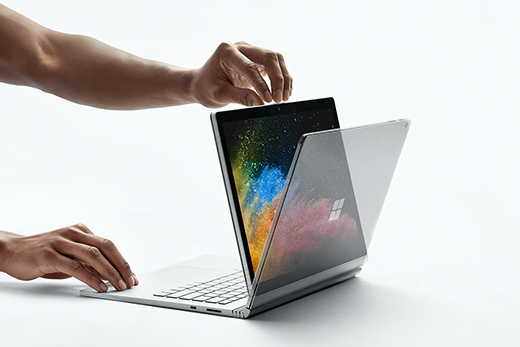 Egy megtekintési módban lévő Surface Book 2 eszközt megnyitó kezeket ábrázoló kép.