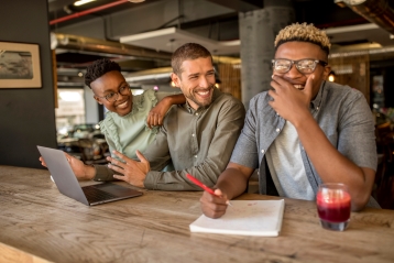 Drie lachende vrienden in een café met laptops