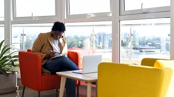 Een vrouw zit voor haar computer op een externe werkplek en maakt notities