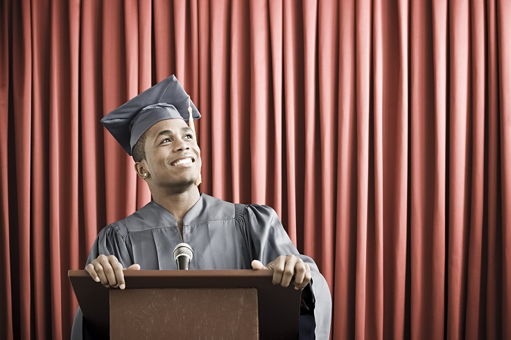 Foto de um jovem vestindo uma túnica de formatura e em pé no pódio.