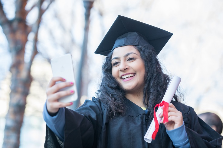 Foto de uma pessoa de boné e gopwn a tirar uma auto-fé de graduação.