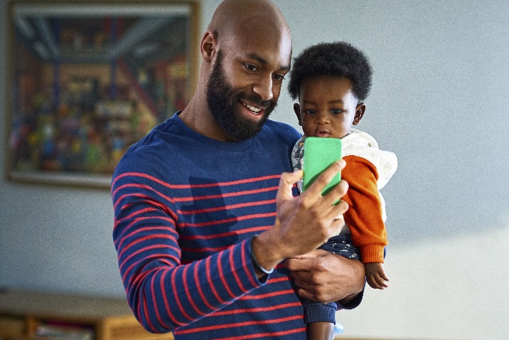 Foto de um homem a segurar uma criança e a falar ao telefone